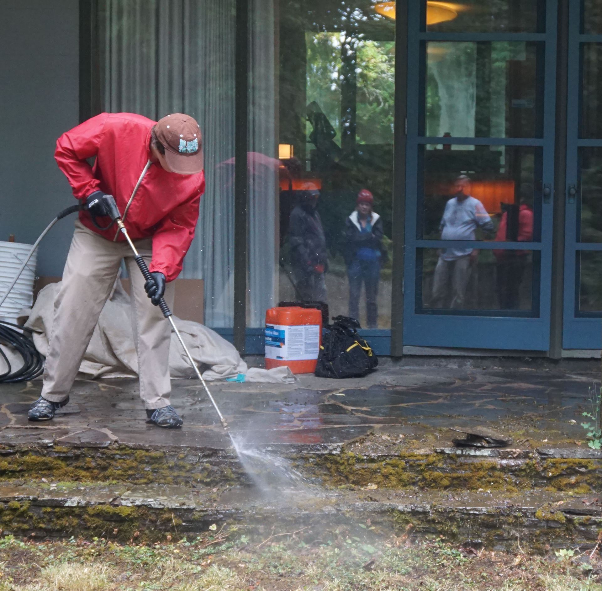 A UO student cleans the back patio stones at the Cottrell house under the watchful eye of the instructors.